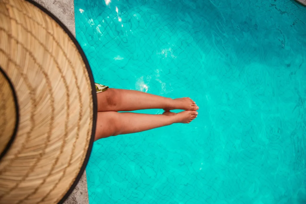 Pernas de uma hóspede na borda de uma piscina de água clara, ao lado de um chapéu de palha; foto de ambiente, o Caminho de Moisés ainda não tem foto própria no acervo