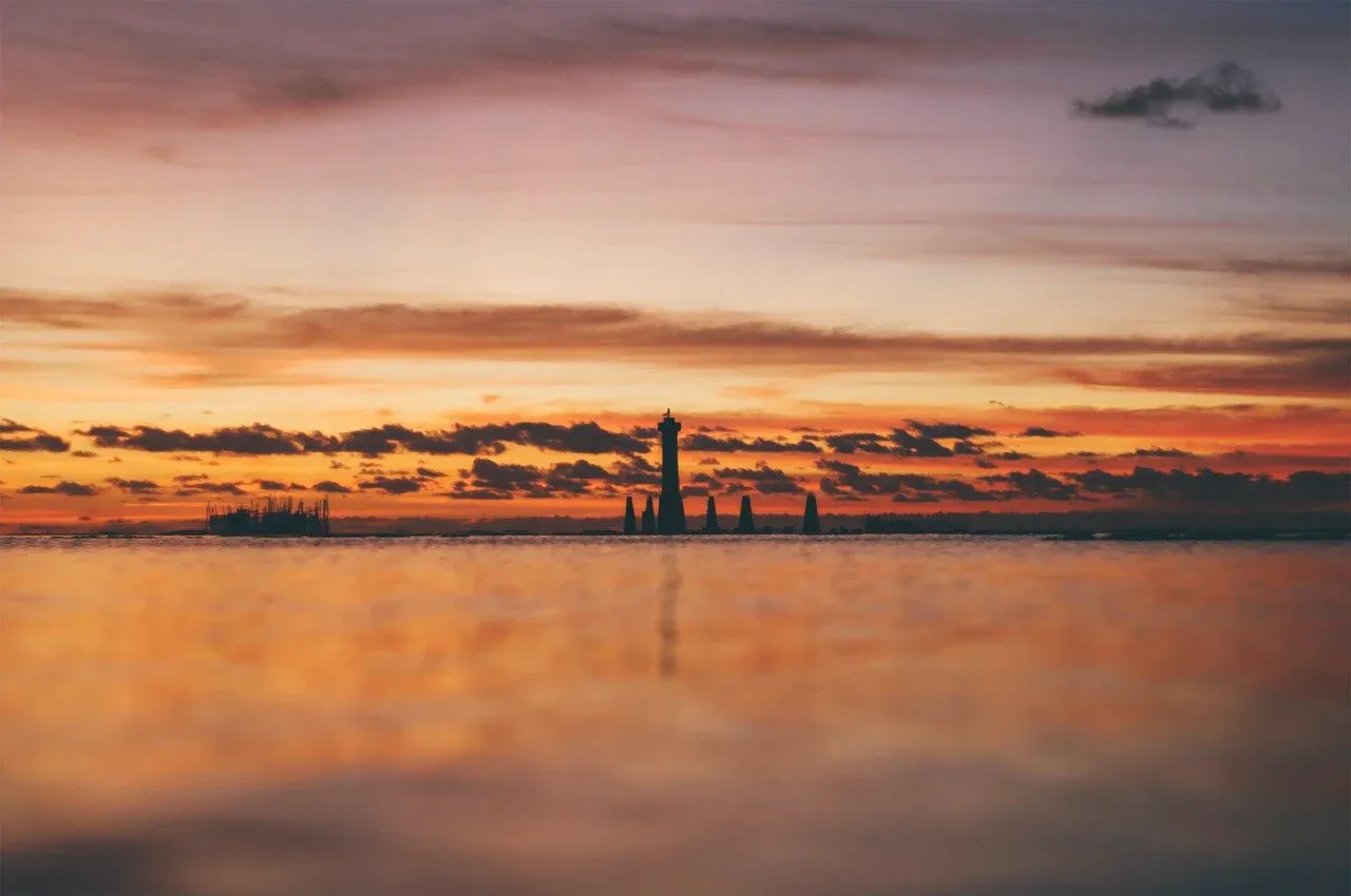 Barco de passeio navegando pela Lagoa Mundaú ao pôr do sol, com manguezais na margem
