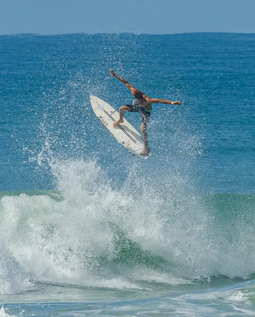 Surfista pegando onda na parte aberta da Praia do Francês, com coqueiros na orla