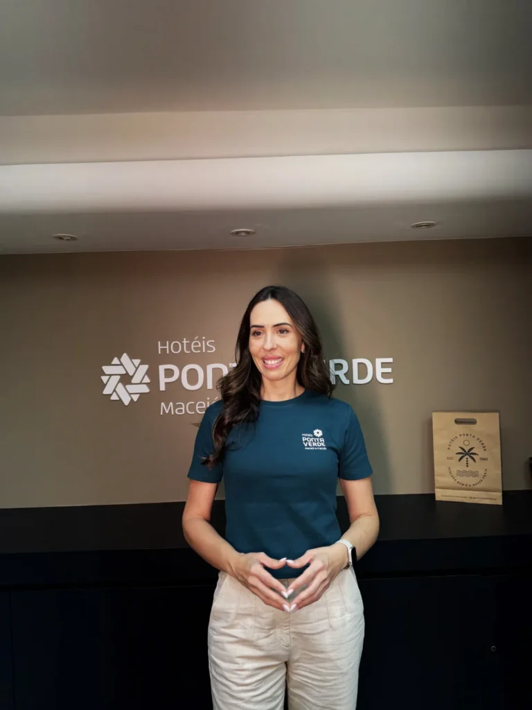 Ana Laura, dos Hotéis Ponta Verde, em frente à marca do hotel em Maceió.