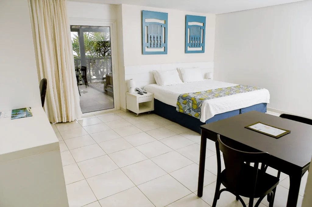 Interior do Garden Premium, no térreo, com cama de casal, mesa e porta de vidro para a varanda com jardim privativo