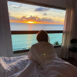 Hóspede na cama do apartamento Frente Mar Casal olhando o mar de Ponta Verde pela janela