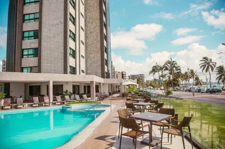 Piscina do Hotel Ponta Verde Maceió com espreguiçadeiras ao sol e a orla de Ponta Verde ao fundo