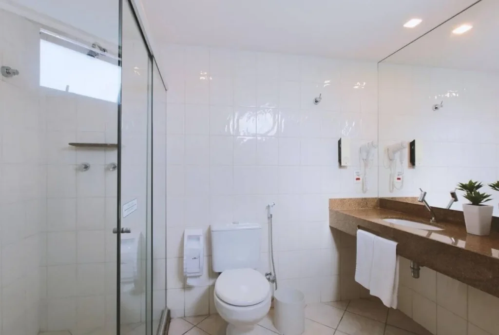 Banheiro do apartamento Standard Duplo, com box de vidro, bancada em granito e secador de cabelo na parede