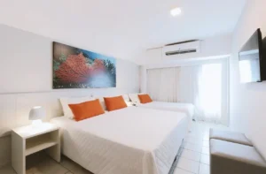 Apartamento Standard do Hotel Ponta Verde Maceió, com cama de casal, cama de solteiro e quadro de coral na parede; foto de ambiente da unidade, o Standard Casal ainda não tem foto própria