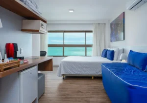 Suíte Superior do Hotel Ponta Verde Maceió com cama ampla e sofá azul, em andar alto frente mar